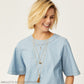 Model wearing layered Brighton gold-tone necklaces with clover pendant, medallion charm, and tassel drop accents