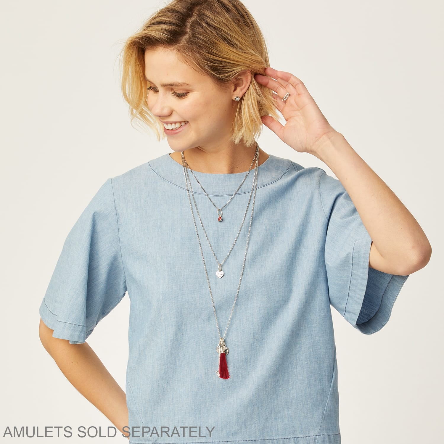 Model wearing Brighton layered silver-tone necklaces with crystal pendant, heart charm, and red tassel accents