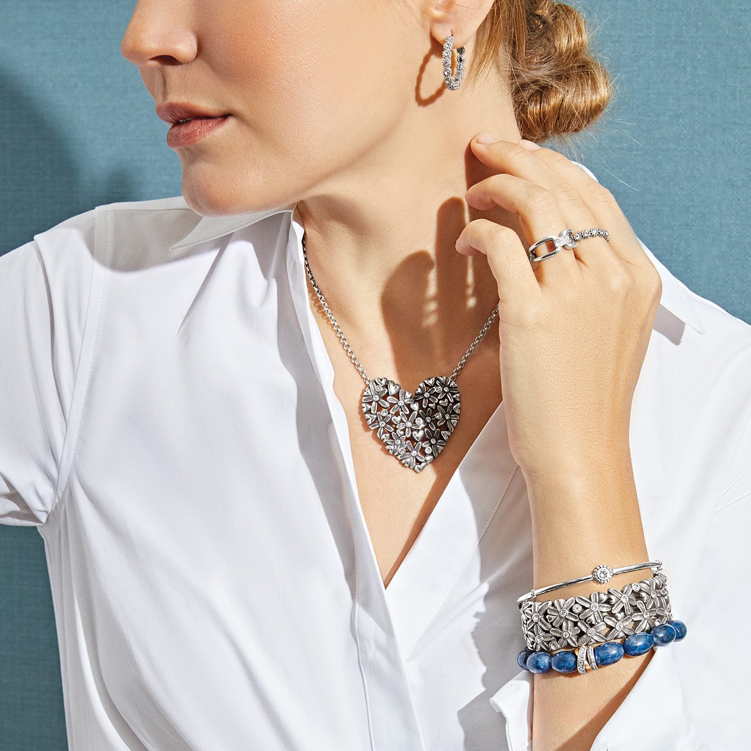 Model wearing a Brighton silver-plated heart necklace with floral design and coordinating Brighton accessories including earrings and bracelets