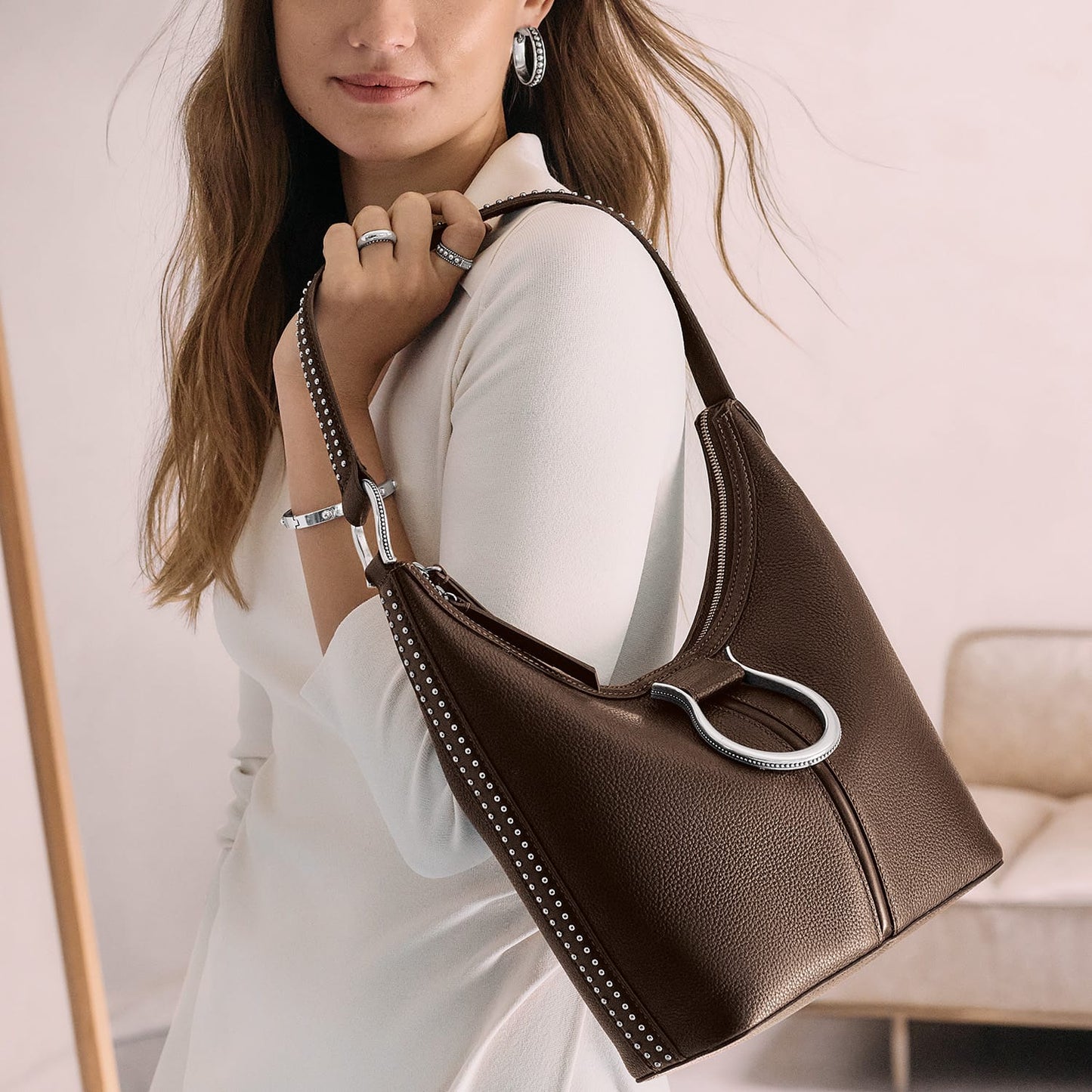 Model with a Brighton brown leather hobo handbag featuring silver-tone studded trim and ring hardware accent