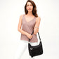 A woman holds a Barbados Ziptop Hobo a black handbag with a heart charm and tassel, dressed in a light brown sleeveless top and white pants, standing against a plain white background.