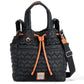 Front view of a Black quilted Kenny Convertible Backpack a handbag with heart patterns and orange drawstrings is standing upright. It has short handles, a detachable shoulder strap with silver buckles, and a front logo plaque.